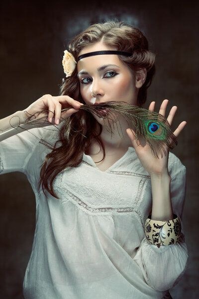 Pretty hippie girl posing with a peacock feather on grunge background
