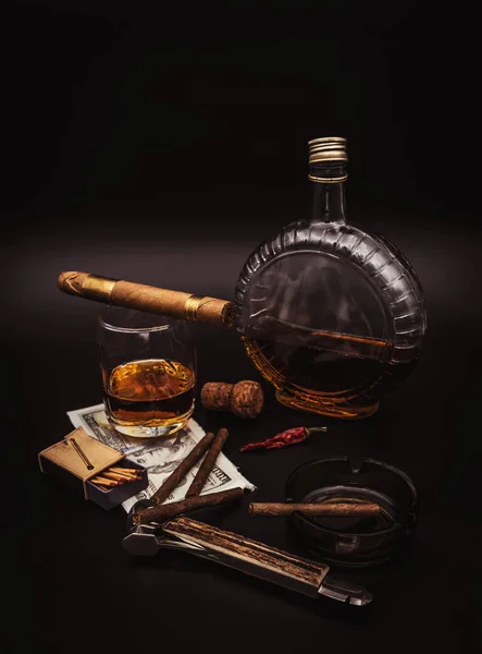 Quality cigars with cognac, cutter, 100 dollar paper, ashtray and red hot pepper on black background