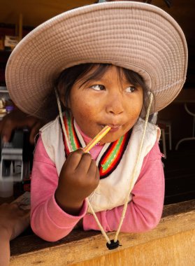 Puno, Peru - October 04, 2021. Portrait of little girl with lollipop and a hat, Titicaca lake in Puno, Peru, South America.