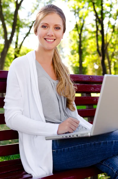 Bionda sorridente seduta nel parco con computer portatile — Foto Stock