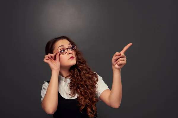 Young curly woman in glasses pointing at empty copyspace — Stock Photo, Image