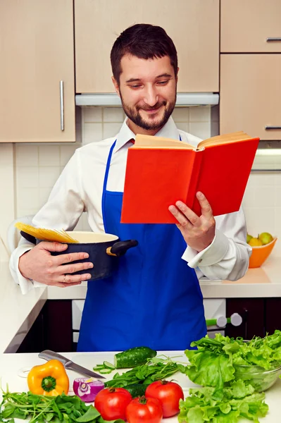 Uomo in grembiule che legge il libro di cucina — Foto Stock