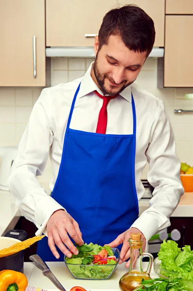 Uomo in grembiule blu preparare insalata fresca — Foto Stock