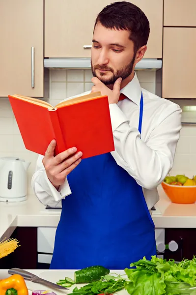 Man in blue apron reading cookbook — Stock Photo, Image