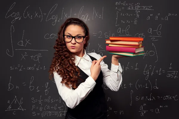 Student with pile of textbooks over chalkboard — Stock Photo, Image