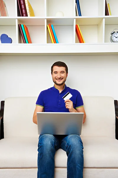 Jovem com laptop e cartão de crédito em casa — Fotografia de Stock