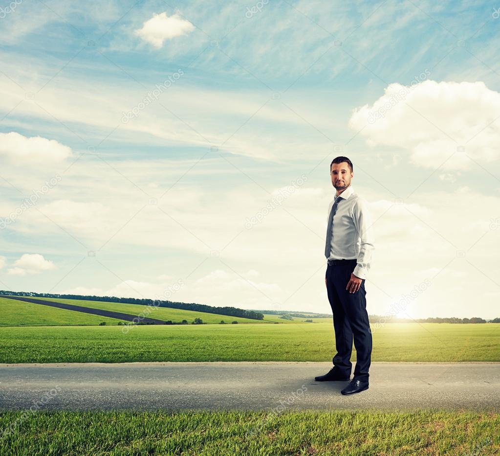 man standing on the road over green field