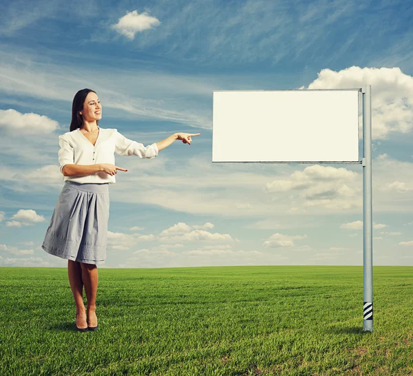 Pretty woman pointing at white billboard — Stock Photo, Image