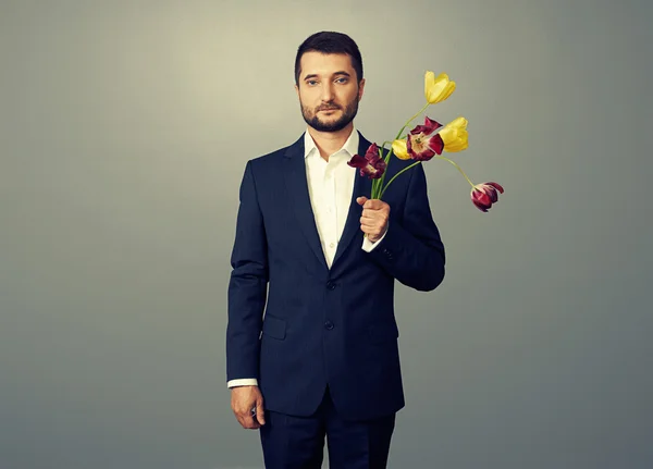 Bel homme avec des fleurs fanées sur sombre — Photo