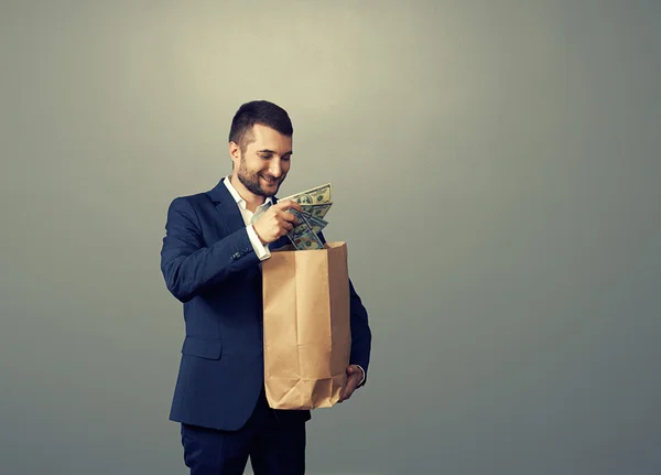Homem com saco de papel e dinheiro sobre escuro — Fotografia de Stock