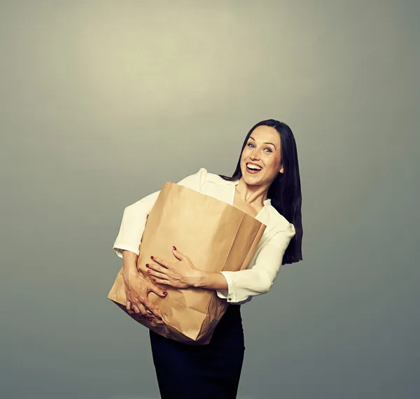 Mulher segurando saco de papel pesado sobre escuro — Fotografia de Stock