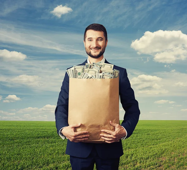 Guapo hombre de negocios sosteniendo bolsa de papel con dinero — Foto de Stock