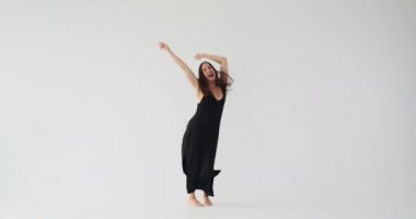 Siyah elbiseli heyecanlı genç kadın atlıyor ve dans ediyor.