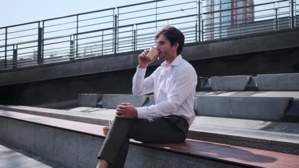Podnikatel pít kávu a pomocí mobilního telefonu sedí na lavičce — Stock video