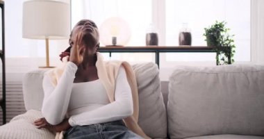 Kanepede oturan Afro-Amerikalı kadın şiddetli baş ağrısı çekiyor.