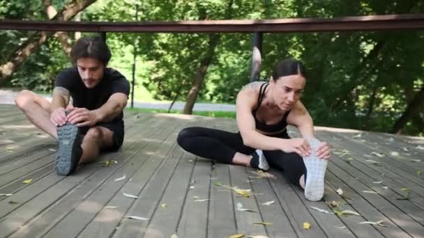 Unga par som gör hand röra tårna från sittande ställning som en stretching övning — Stockvideo