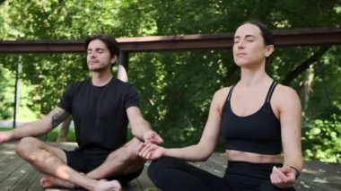 Lotus yogasında oturan genç çift gözleri kapalı poz veriyor.