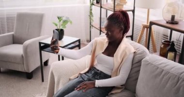 Afro-Amerikalı kadın evde cep telefonu kullanarak görüntülü sohbet yapıyor.