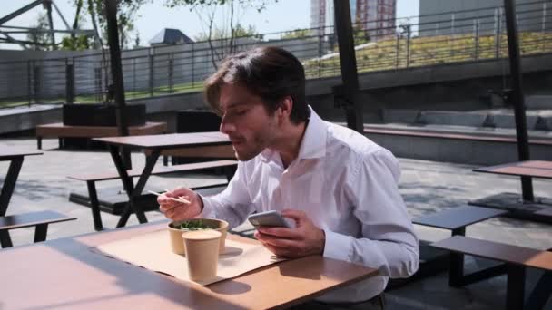 Genç adam yemek yerken cep telefonu kullanıyor. — Stok video
