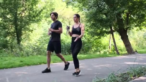 Jeune couple en vêtements de sport boire de l'eau tout en marchant sur la route — Video