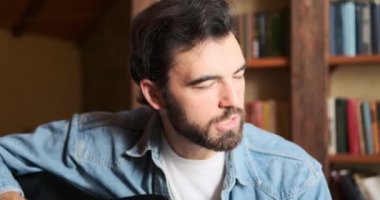 Adam evde şarkı söylüyor ve gitar çalıyor.