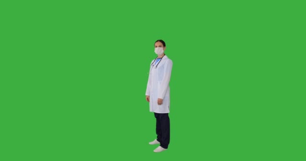 Kobieta lekarz noszenie maski medycznej twarzy i gestykulując ok znak na zielonym tle — Wideo stockowe