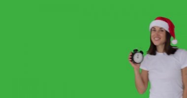 Noel Baba şapkalı mutlu kadın çalar saatin saatini gösteriyor.