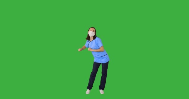 Kvinnlig sjuksköterska bär skyddande ansiktsmask och dansa över grön bakgrund — Stockvideo