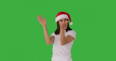 Noel Baba şapkalı heyecanlı kadın yeşil arka planda alkışlıyor.