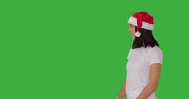 Kırmızı Noel Baba şapkalı kadın yeşil arka planı işaret ediyor.