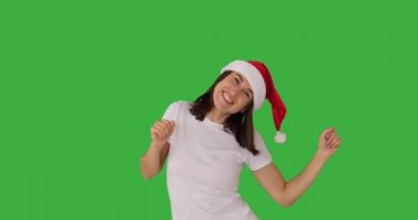 Noel Baba şapkalı kadın yeşil arka planda dans ediyor.