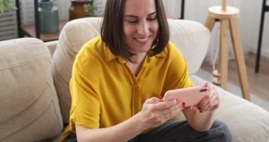 Cep telefonu kullanan ve evdeki koltukta dans eden bir kadın.