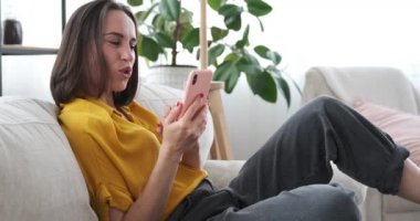 Evdeki koltukta cep telefonu kullanarak öpüşen bir kadın.