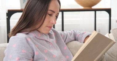 Evdeki kanepede kitap okuyan kadın.