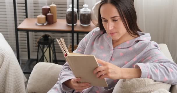 Mujer leyendo un libro en el sofá en casa — Vídeos de Stock