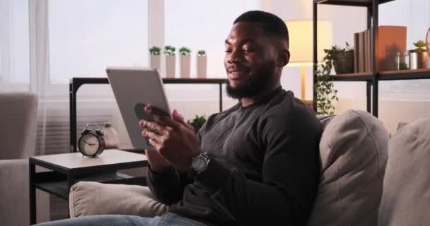 Uomo seduto sul divano e utilizzando tablet digitale — Video Stock
