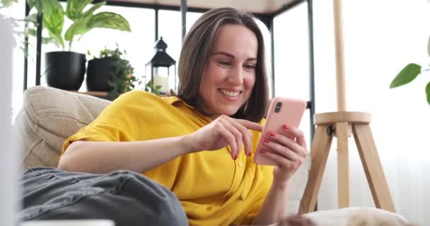 Женщина с мобильного телефона лежит на диване дома — стоковое видео
