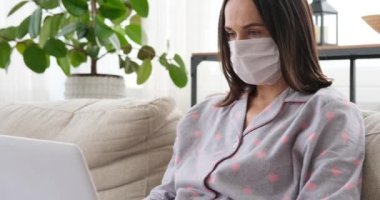 Koruyucu yüz maskesi takan bir kadın evde dizüstü bilgisayarla çalışıyor.