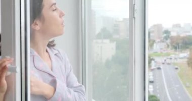 Kadın evinin penceresinden temiz hava solumak için maskesini çıkarıyor.
