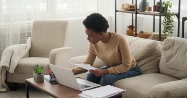 Evrakları analiz eden ve evde dizüstü bilgisayar kullanan kadın.