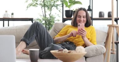 Evdeki koltukta uzanmış cep telefonu kullanan bir kadın.