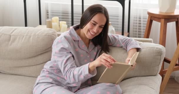 Szczęśliwa kobieta czyta książkę o sofie w domu — Wideo stockowe