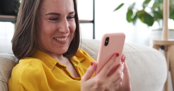 Vrouw met mobiele telefoon op de bank thuis — Stockvideo