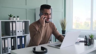 Ofiste cep telefonu ve laptop kullanan bir işadamı.