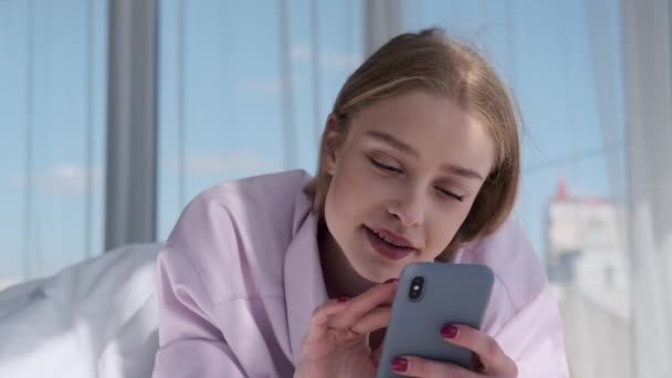 Красива жінка посміхається під час використання мобільного телефону на ліжку — стокове відео