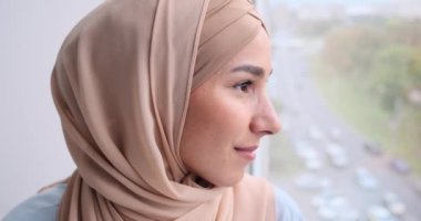 Arap kadın gülümsüyor ve pencereden dışarı bakıyor.