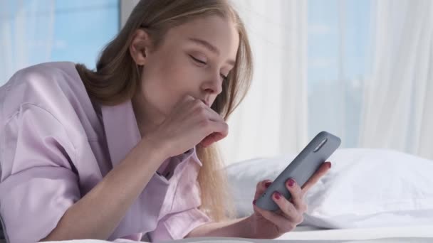 Ευτυχισμένη νεαρή γυναίκα που χρησιμοποιεί το κινητό τηλέφωνο στο κρεβάτι — Αρχείο Βίντεο