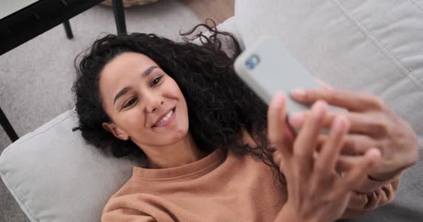 Femme heureuse couchée sur le canapé et prenant selfie en utilisant un téléphone mobile — Video