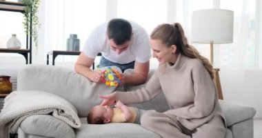 Parents playing with rattle over baby son lying on sofa