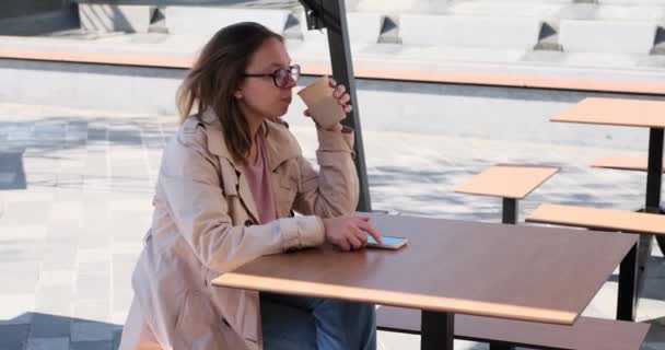Νεαρή γυναίκα μιλάει στο κινητό ενώ πίνει καφέ — Αρχείο Βίντεο